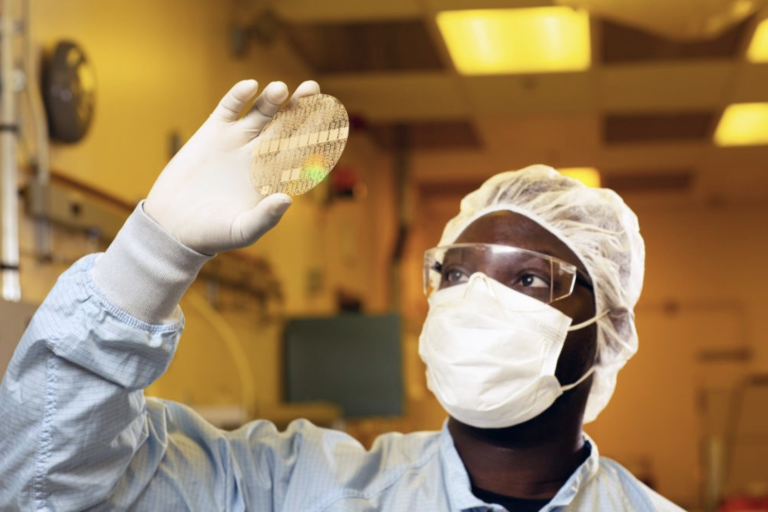 Technician examining diamond wafer substrate under cleanroom conditions with protective equipment
